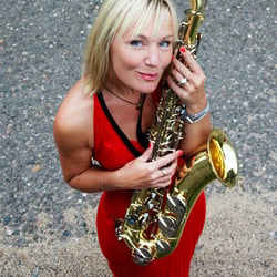 DJane Simoné lächelt und hält Saxophon im Arm.