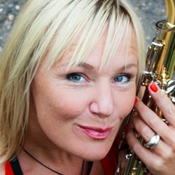 DJane Simoné lächelt und hält Saxophon im Arm.