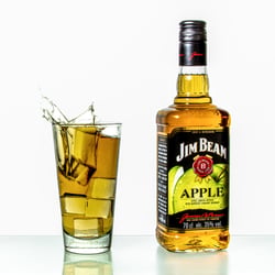 Spritzer mit einem Eiswürfel in einem Glas Bourbon Whisky. Bourbon whiskey splashes with an ice cube in a glass